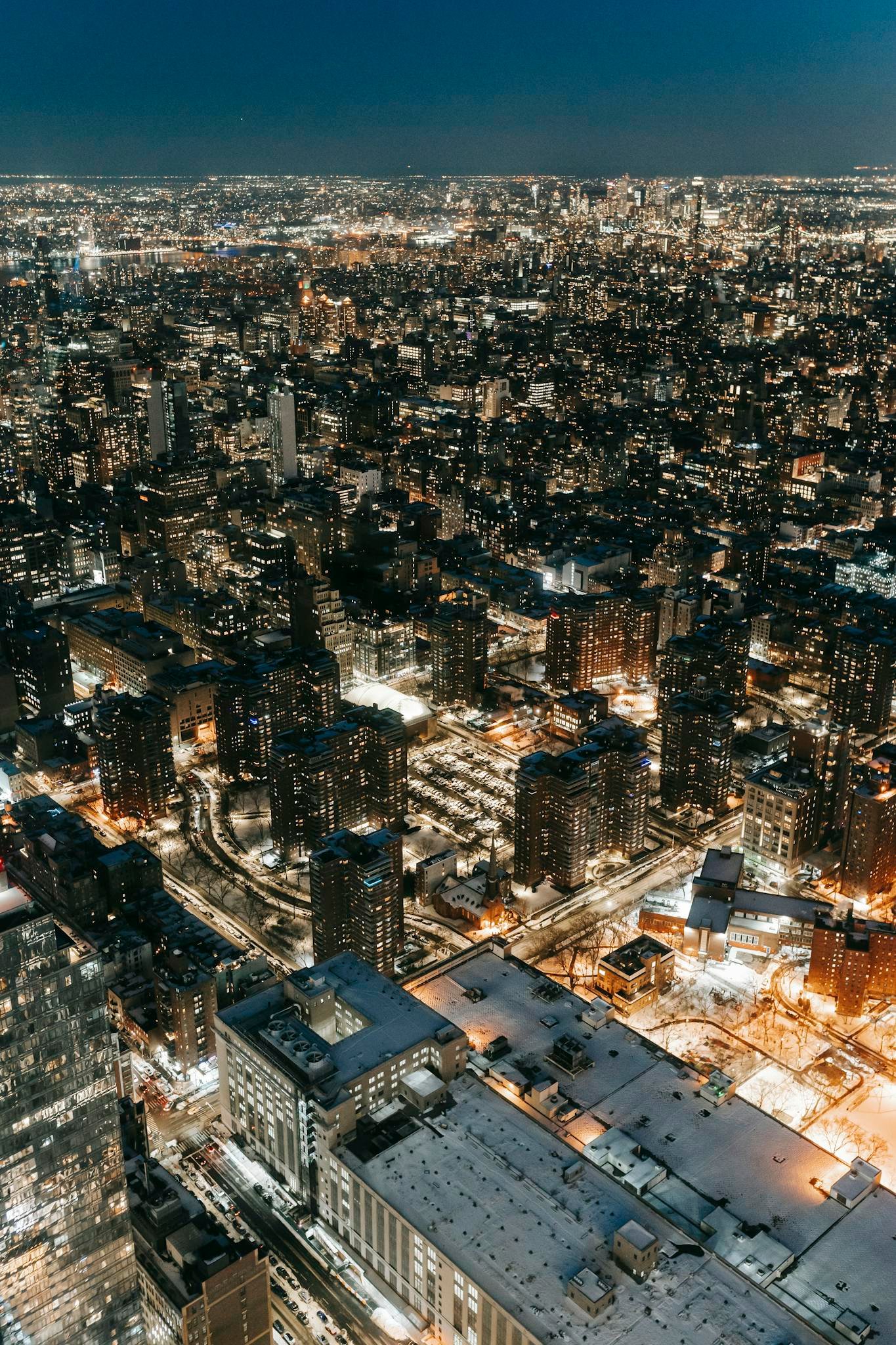 Drone view of contemporary multistory buildings with glowing lights located on streets with road of modern city at night time